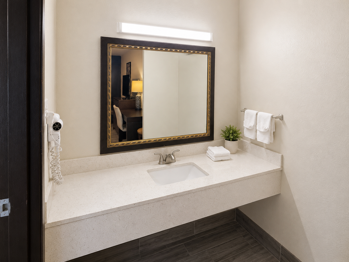 Small restroom vanity with mirror, sink, towel ring, and wall light above a speckled countertop.