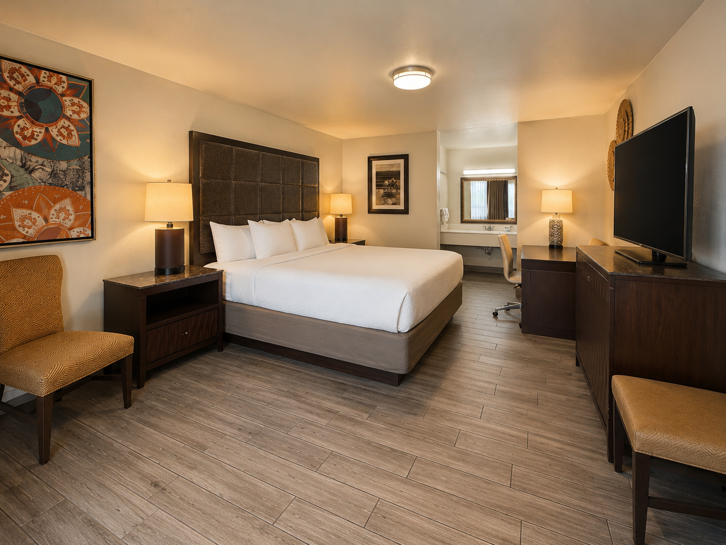 Hotel room with a king bed, two nightstands, wall-mounted TV, and warm lighting