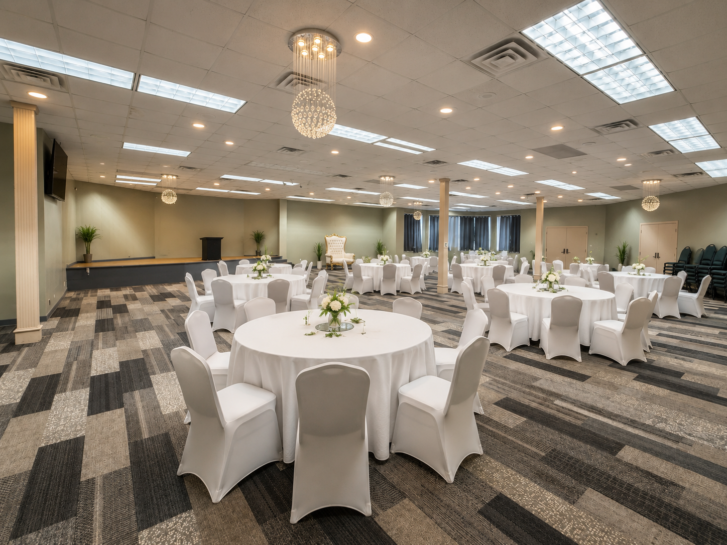 Elegant banquet hall with round, white-clothed tables and chair covers under bright ceiling lights