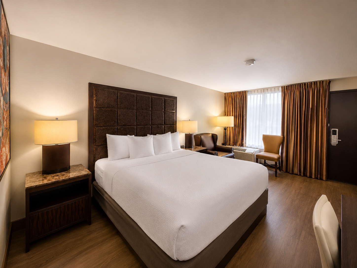 Modern hotel room with a bed, bedside lamp, desk, chair, and curtains