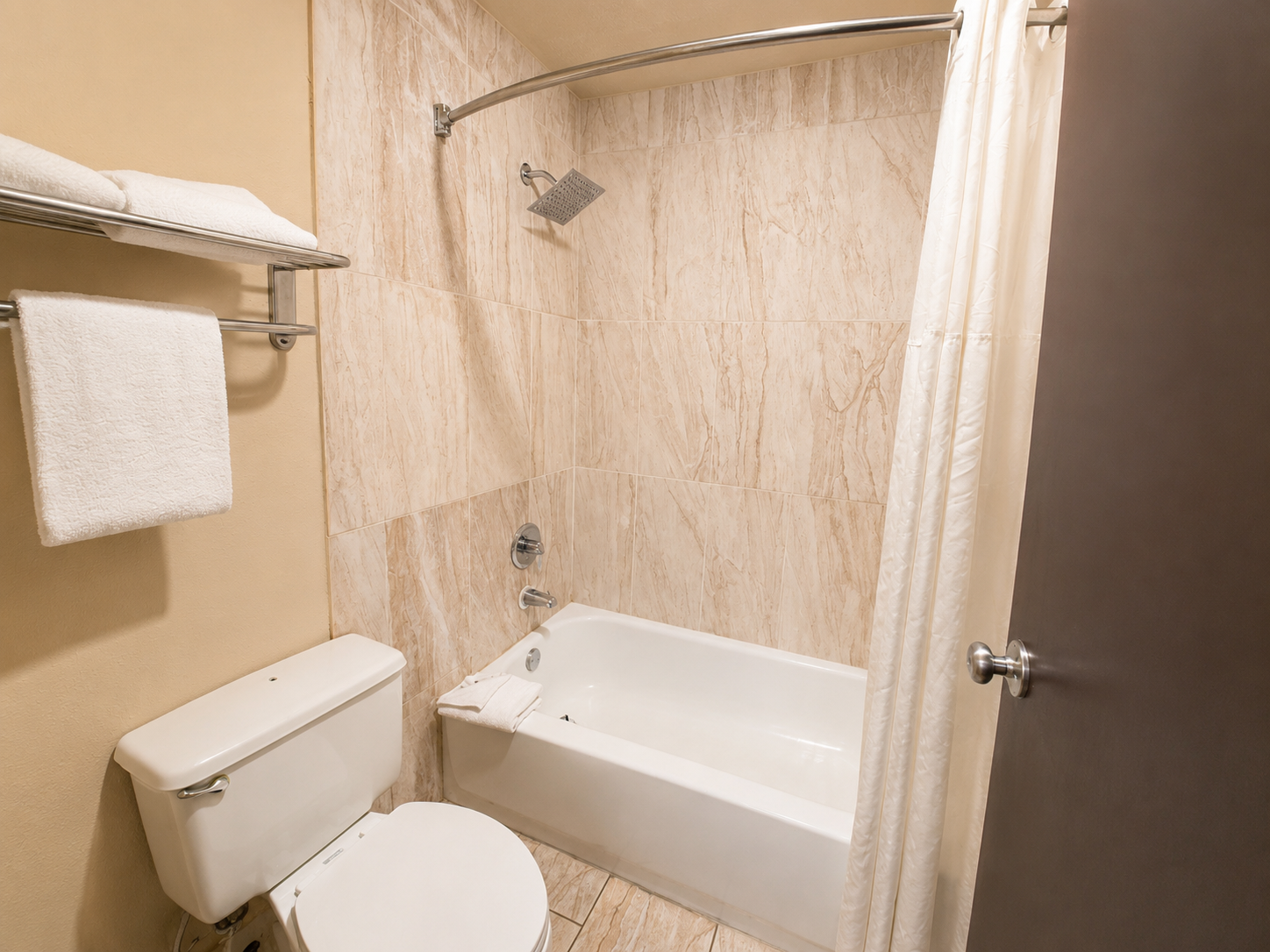 Small beige bathroom with toilet, bathtub-shower combo, towel rack, and open door.