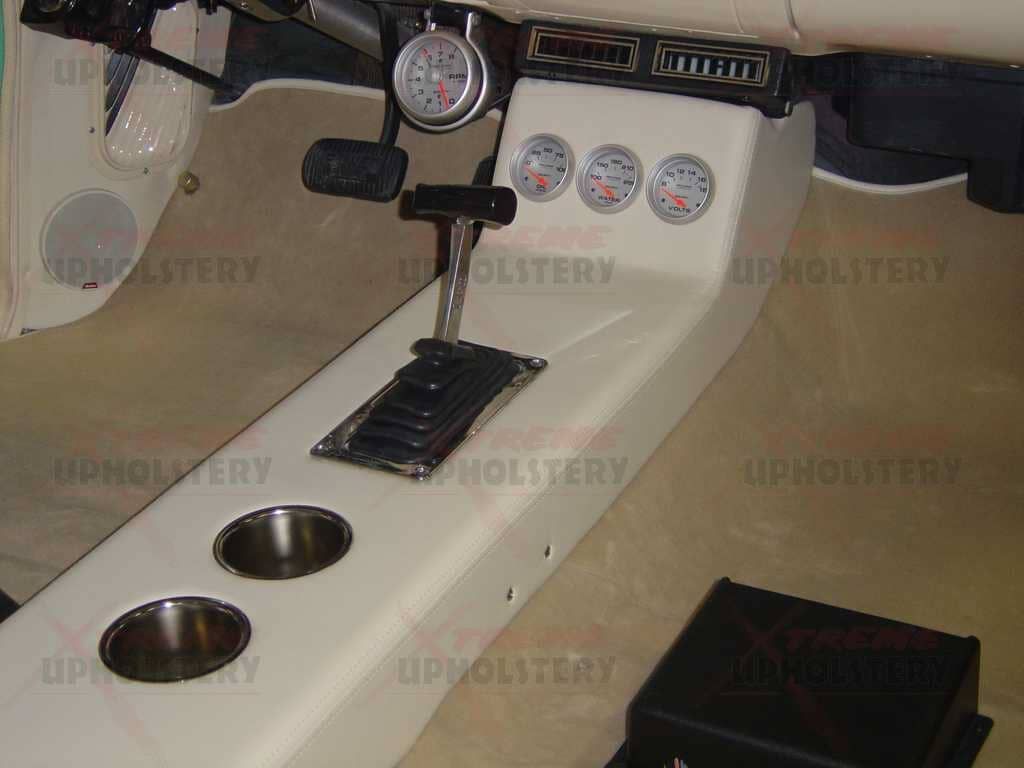 Car interior with cream console, cup holders, gauges, shifter, and black speaker box