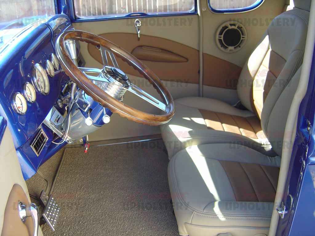 Vintage car interior with tan bench seat, blue dashboard, and wood steering wheel