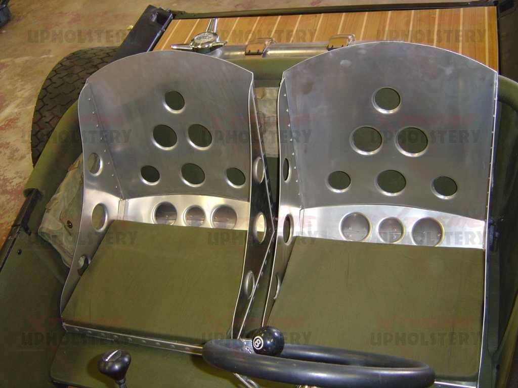 Two metallic car seats with circular cutouts, shown side by side in a workshop setting.
