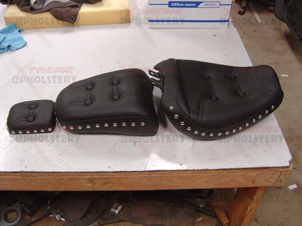 Black leather saddle bags and a matching pouch on a white worktable in a workshop