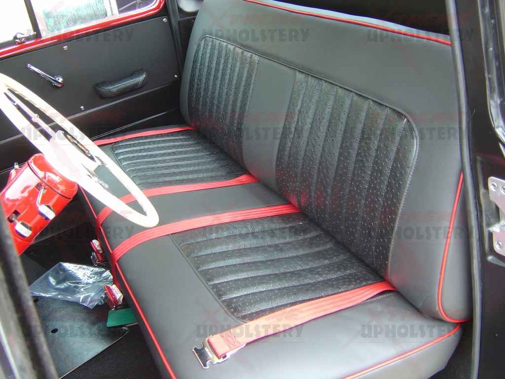 Vintage car interior with black bench seat, red trim, and white steering wheel