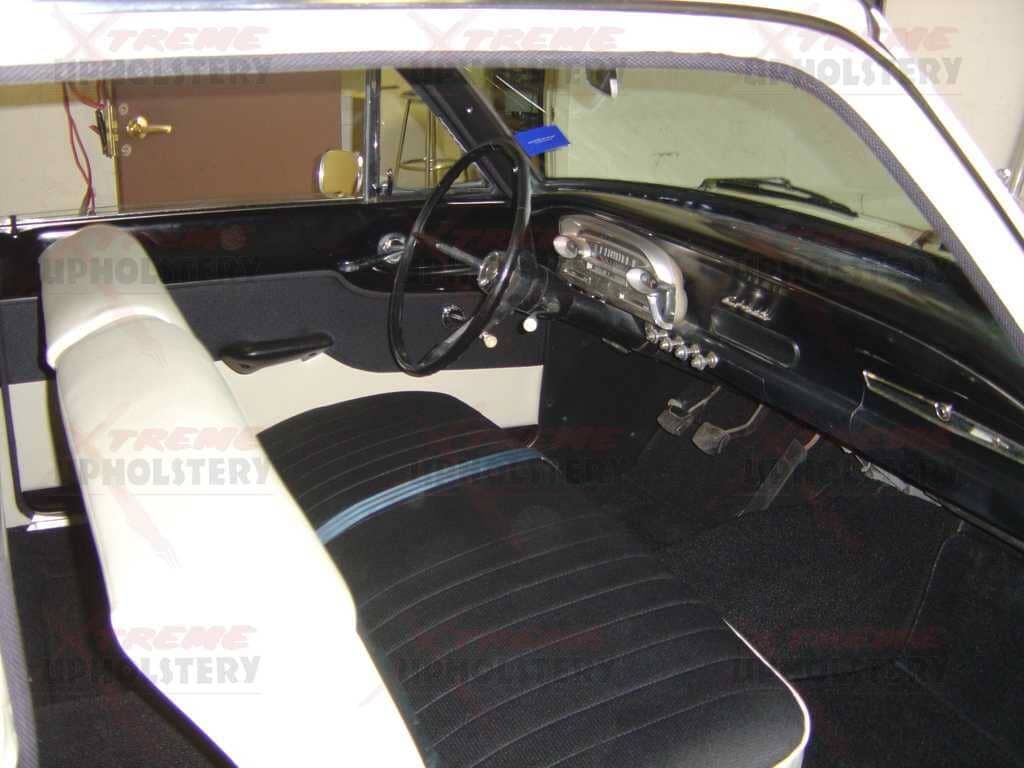 Vintage car interior with black-and-white bench seat and dashboard, viewed from the open passenger side