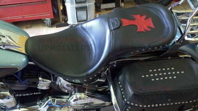 Black leather motorcycle seat with red emblem, next to a studded black saddlebag in a garage