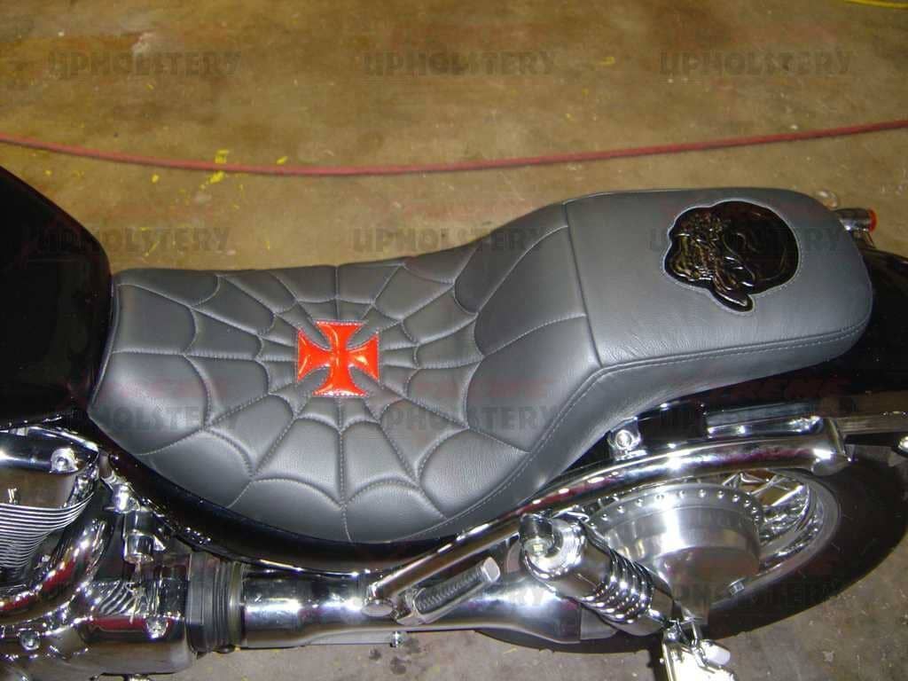 Black motorcycle seat with quilted pattern and orange emblem, viewed from above