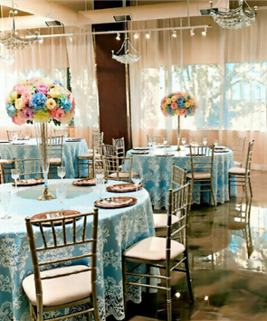 Wedding reception hall decorated with blue and white flowers and chandeliers. Tables set.