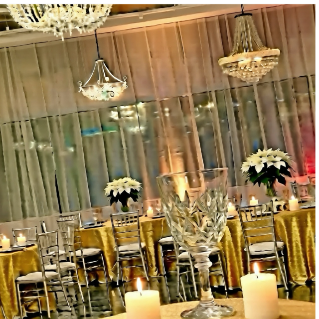 Elegant event venue with gold tablecloths, clear chairs, chandeliers, and candles.