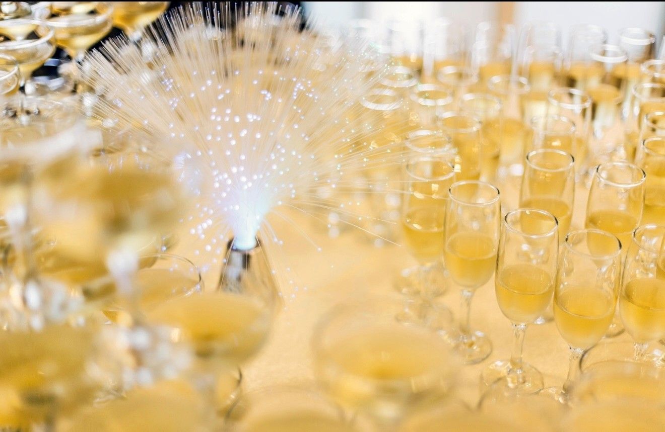 Elegant event hall set for a celebration. Round tables with floral centerpieces, purple and white draping, chandeliers.
