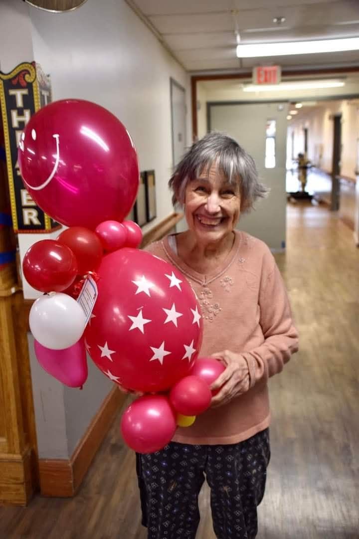 Smiling woman holding pink balloons in a hallway