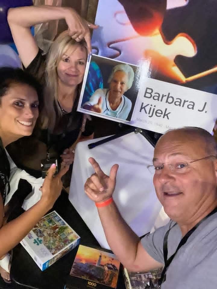 Group selfie at an event, with a sign reading “Barbara J. Kijek” and people smiling beside it