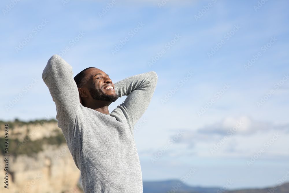 Man with arms behind head, smiling at sky. Outdoors, sunny day.