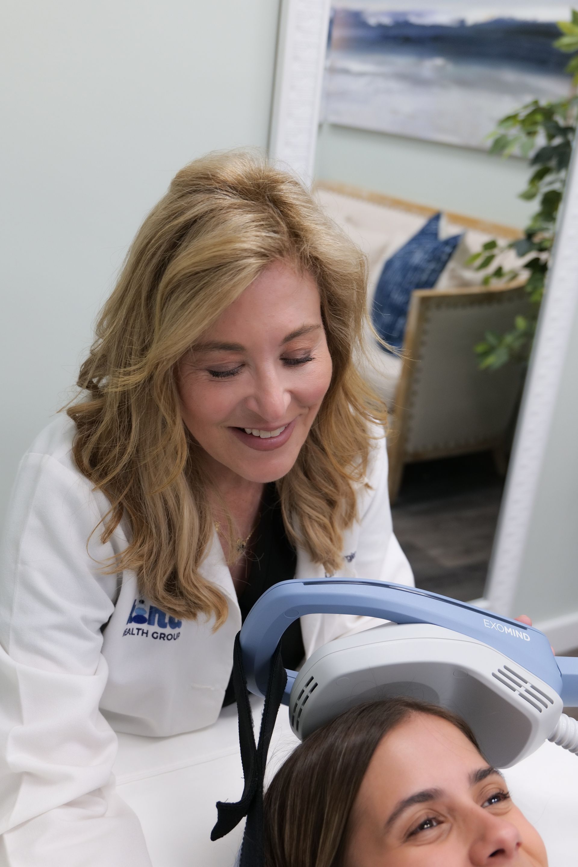 Woman in lab coat operates medical device on patient's head in a clinic.