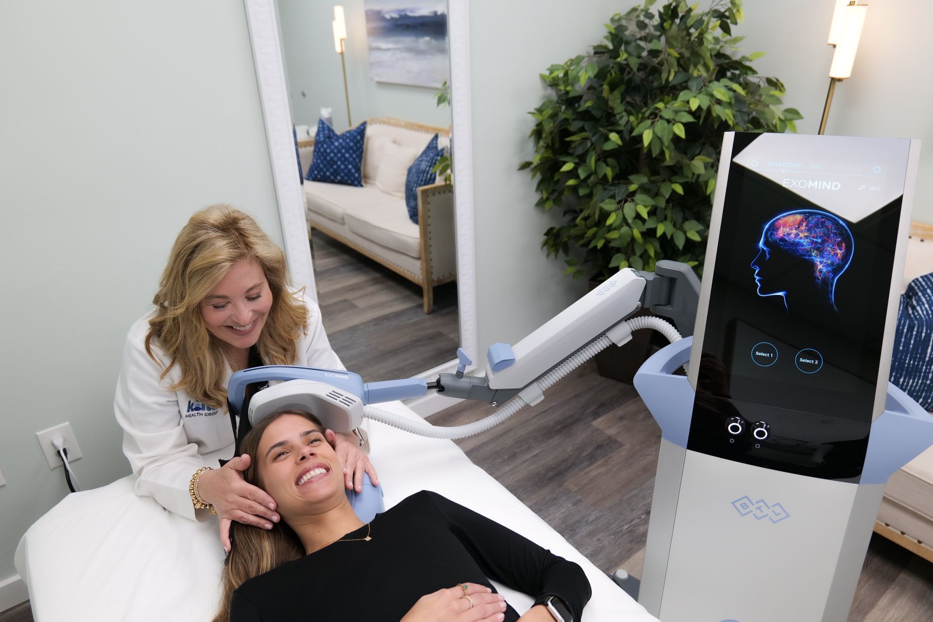 Woman receives brain therapy from a medical professional in a treatment room; brain scan displayed on machine.