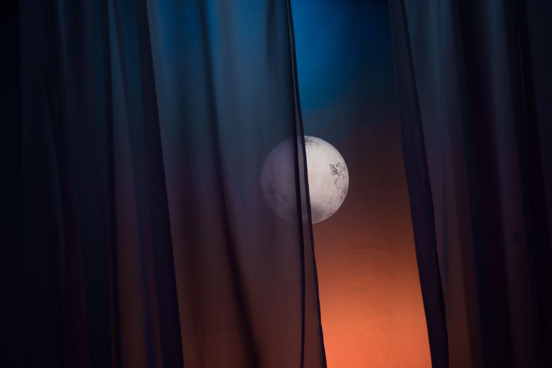 Moon peeking through dark curtains at dusk, with an orange glow in the background