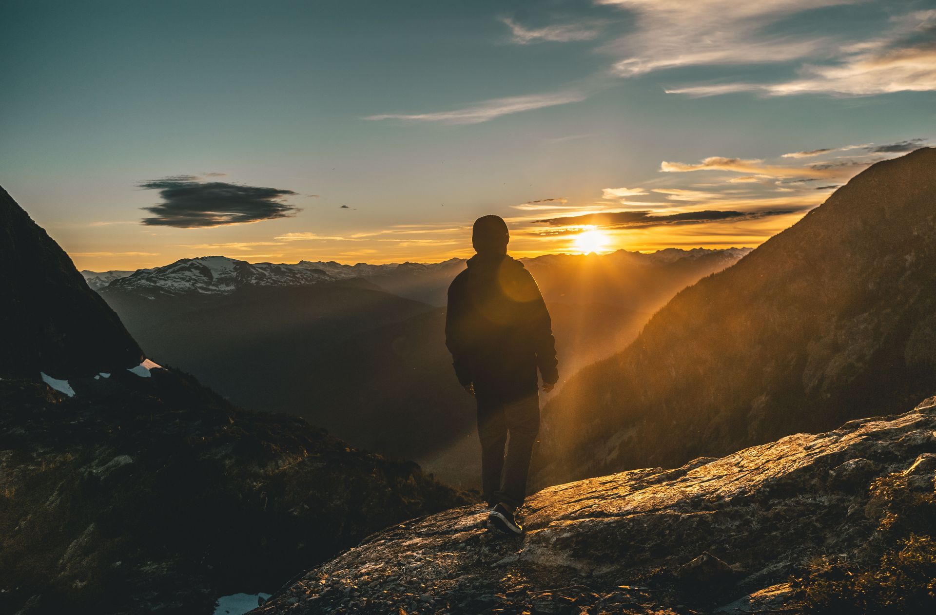 Silhouetted hiker on a mountain ridge at sunset, overlooking a valley with golden light