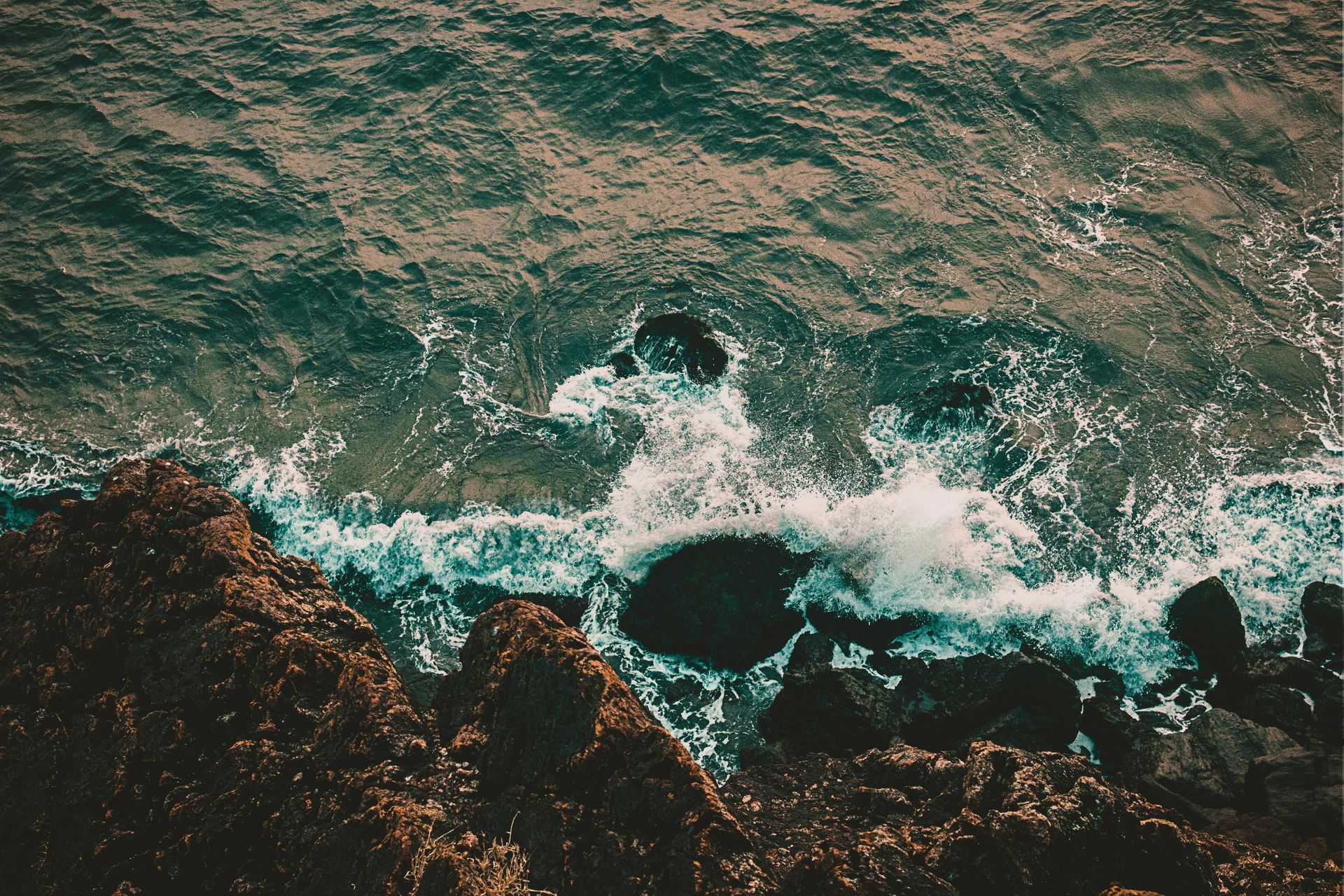 Rough, teal ocean waves crashing against dark, rocky shore.