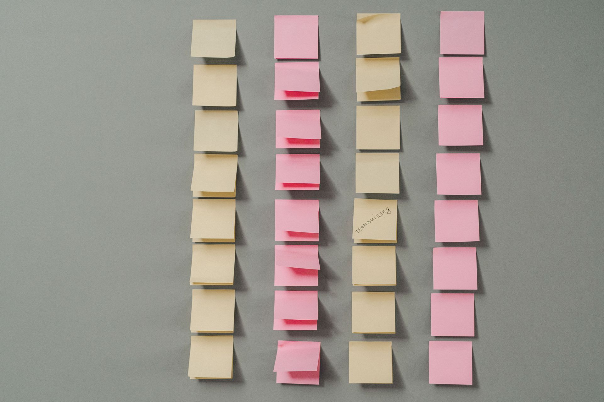Four vertical columns of stacked beige and pink sticky notes on a gray surface