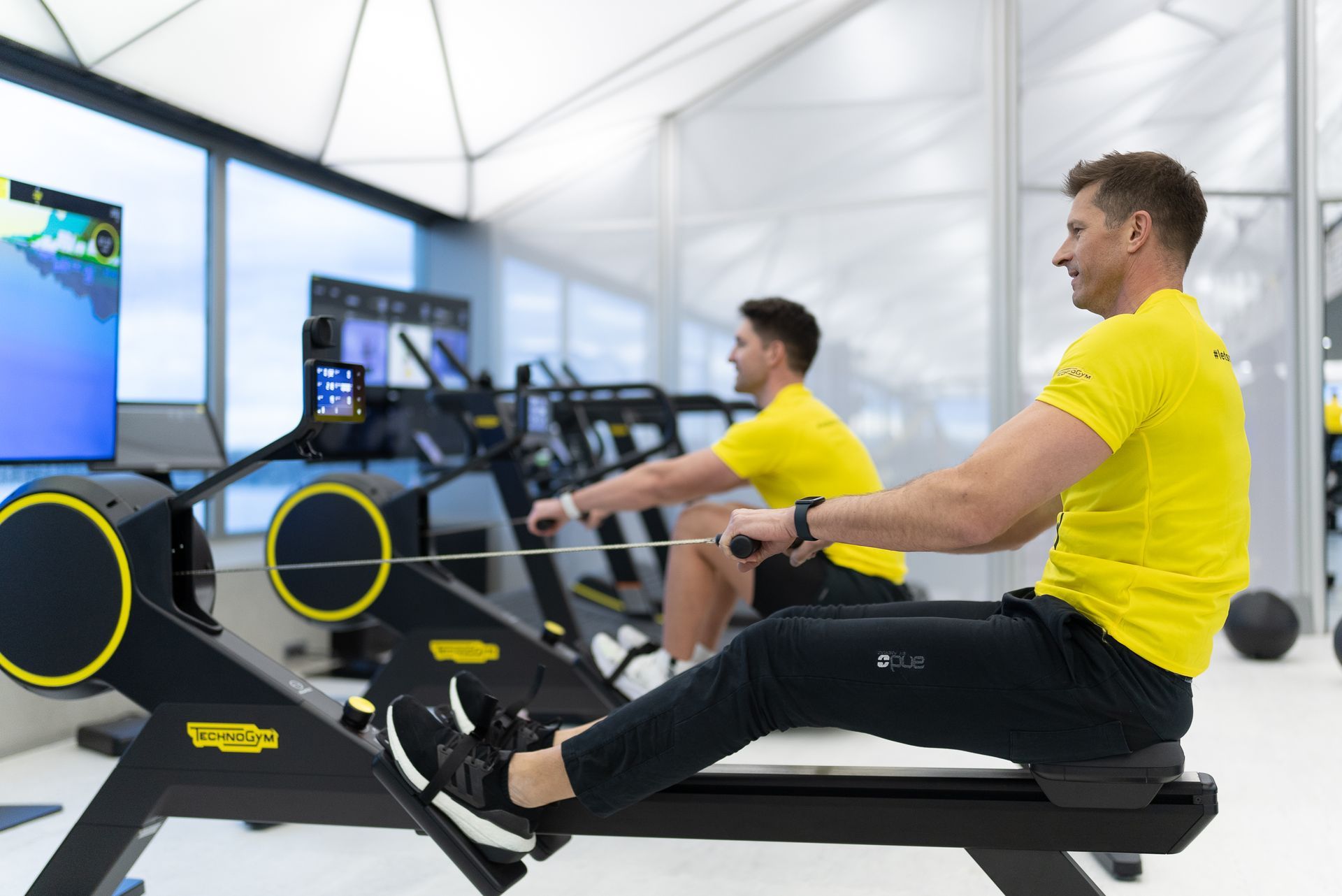 two men are rowing machines in a gym .