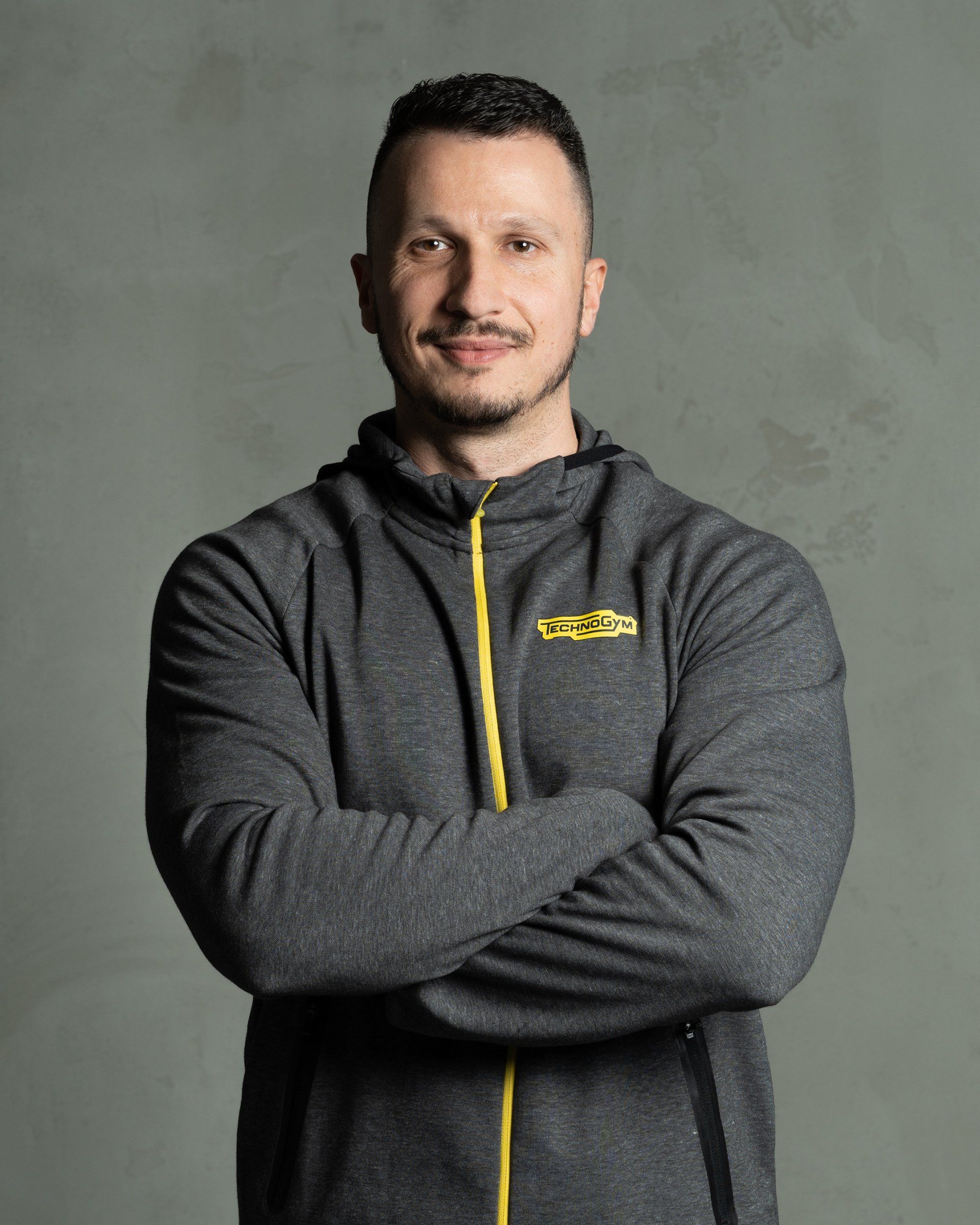 a man with his arms crossed is wearing a grey jacket with a yellow zipper