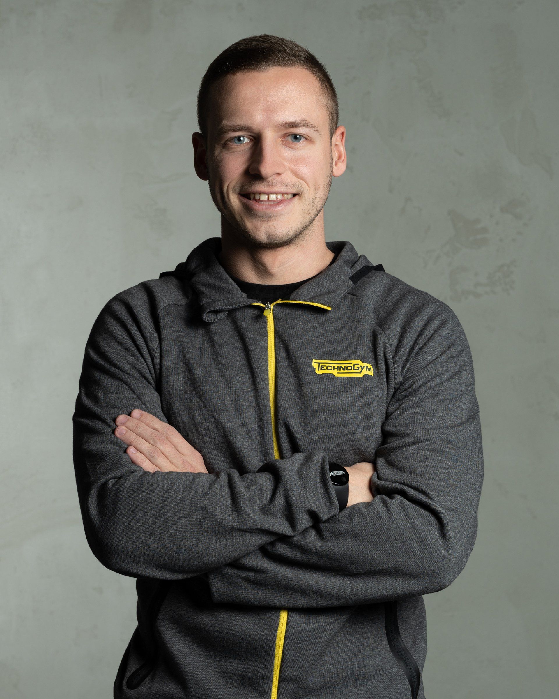 a man with his arms crossed is wearing a grey jacket with the word technogym on it