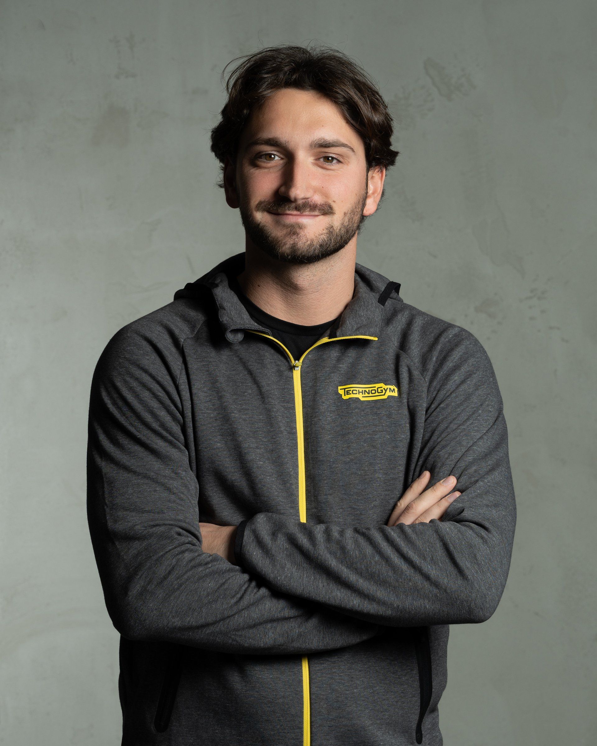 a man with his arms crossed is wearing a grey jacket with a yellow zipper