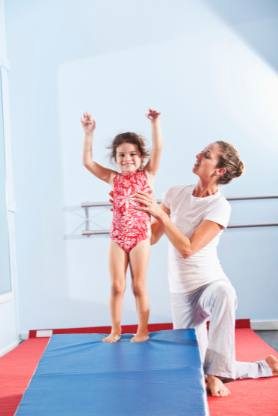 A woman is helping a little girl balance on a balance beam.