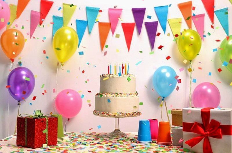 A birthday party with a cake , balloons , gifts and confetti.