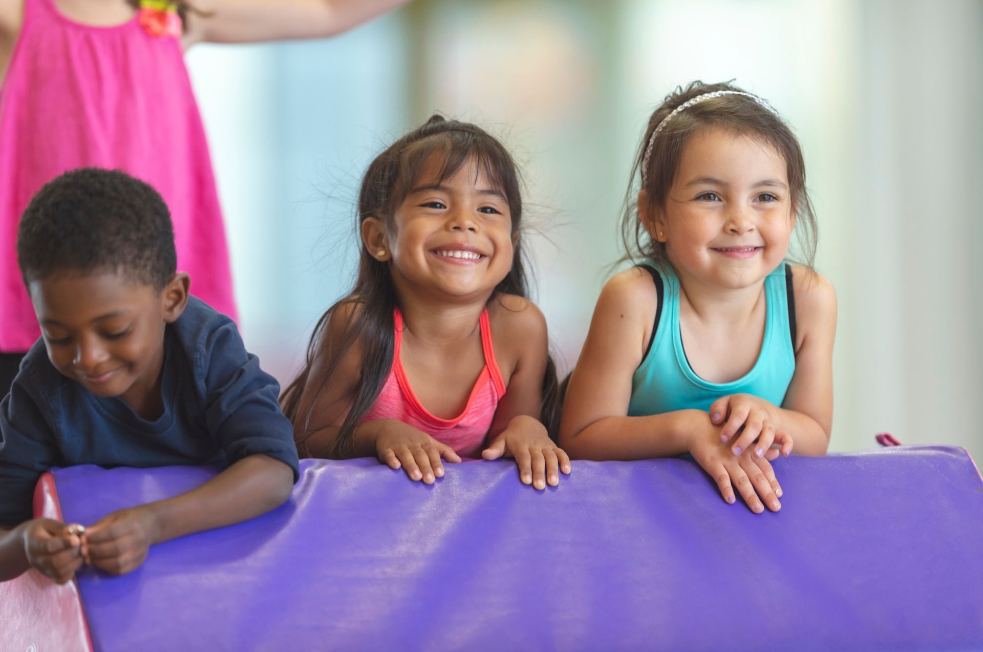 A group of children are laying on a purple mat and smiling.