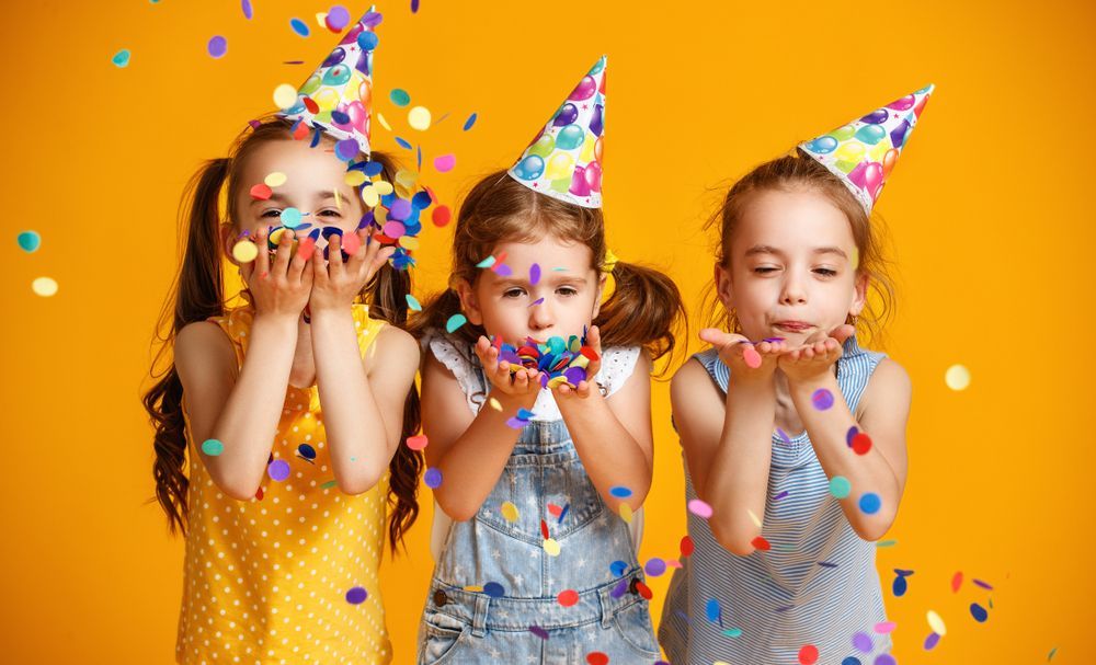 Three little girls are blowing confetti at a birthday party.
