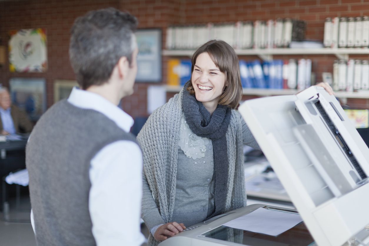 Two people smiling and talking at a computer in a library or office setting