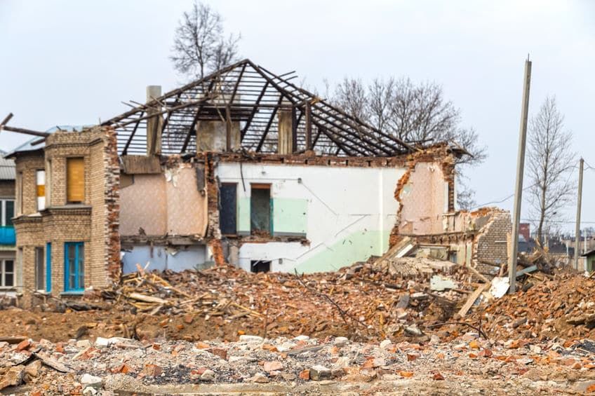 Partially destroyed house with collapsed roof and debris after damage or demolition