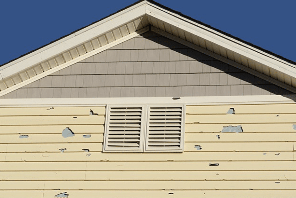 Yellow house siding with peeling paint, a vent, and gray triangular gable.