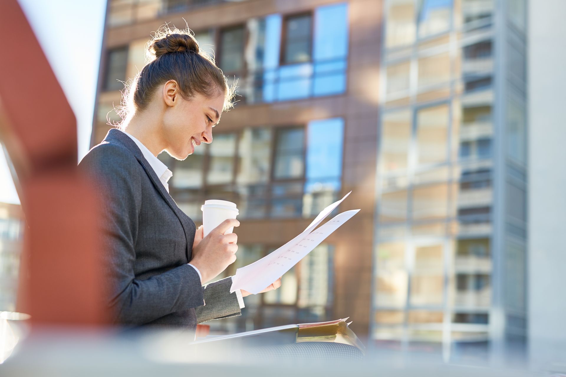 Woman wearing glasses at construction site, holding files, looking at the building.