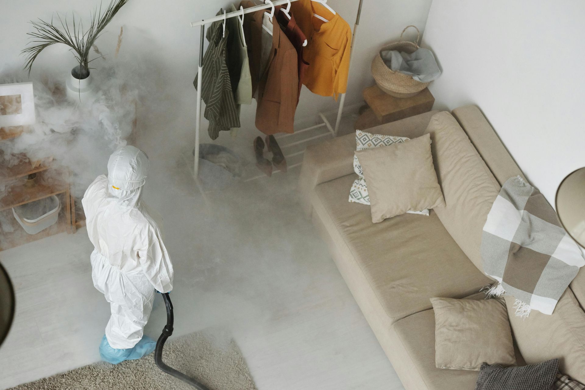 Person in hazmat suit disinfecting a living room with fog.