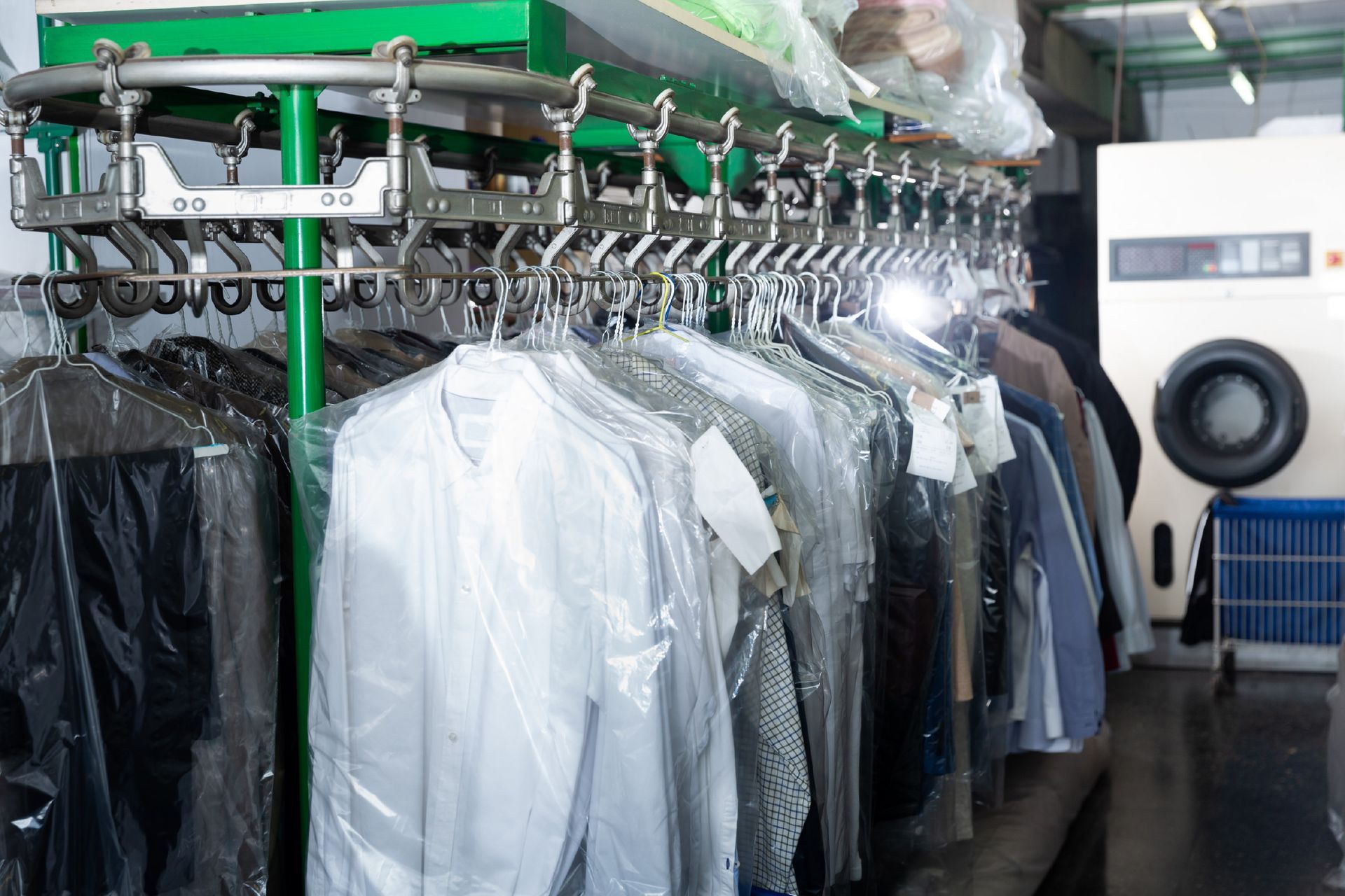 A motorized clothing conveyor rack in a dry cleaner filled with garments protected by clear plastic covers.