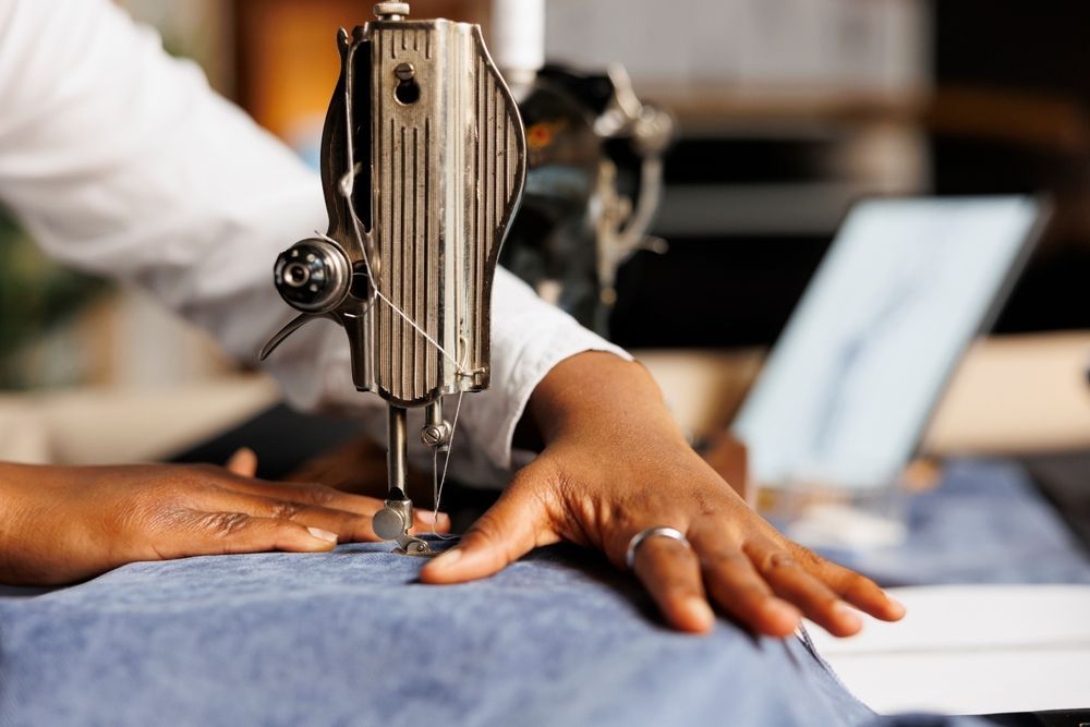 Hands measuring fabric with a blue tape measure on a worktable