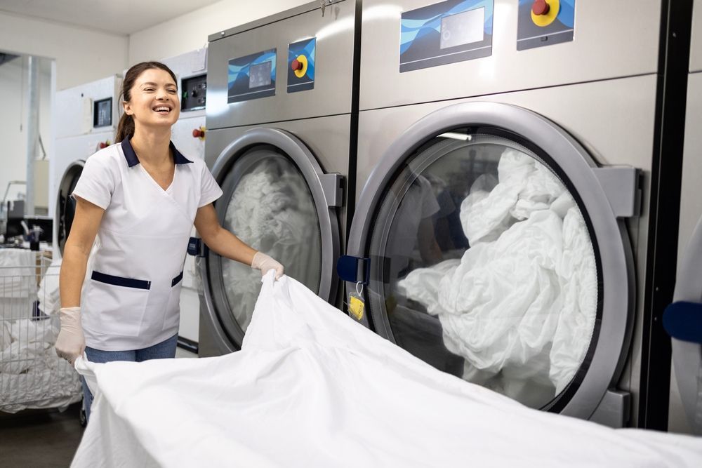 Laundry worker loading white linens into industrial washing machines
