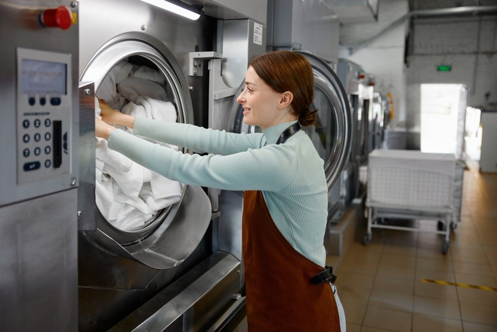 Worker loading laundry into a large industrial washing machine in a laundry facility