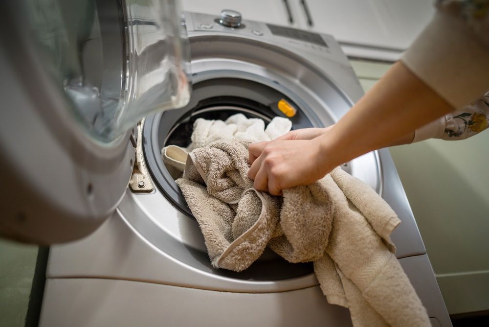 Hand loading a beige towel into a front-loading washing machine
