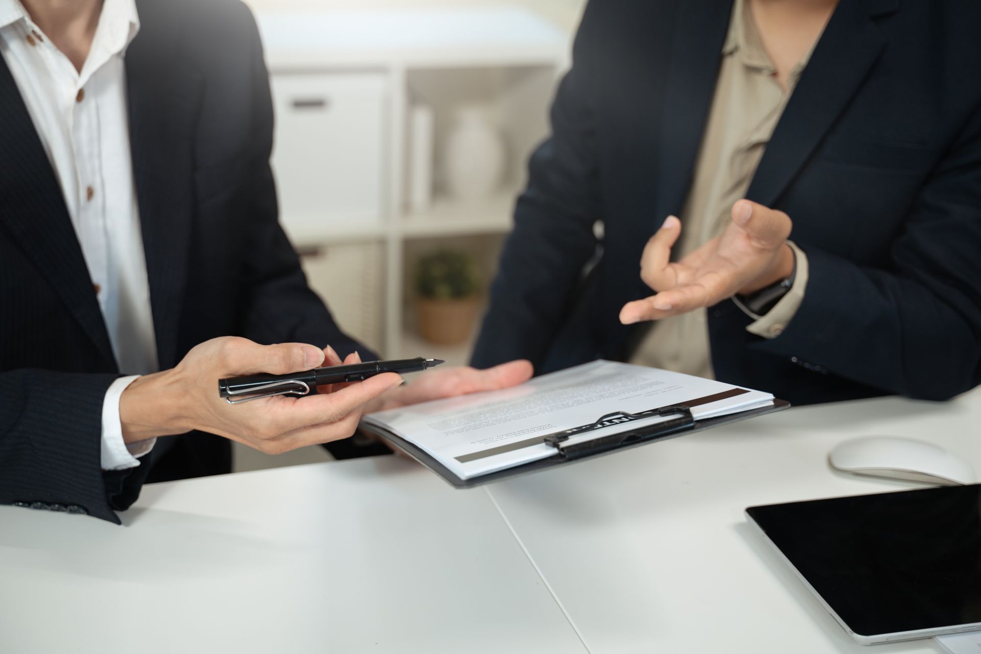Two people in business attire exchanging keys and documents at a meeting table.