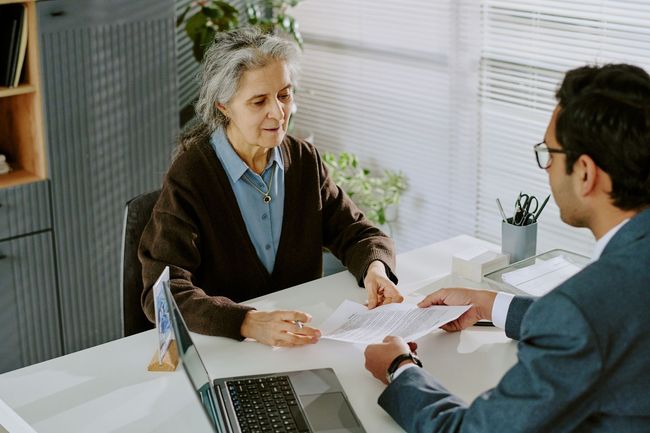 Two people in a meeting across a desk, reviewing papers in a bright office