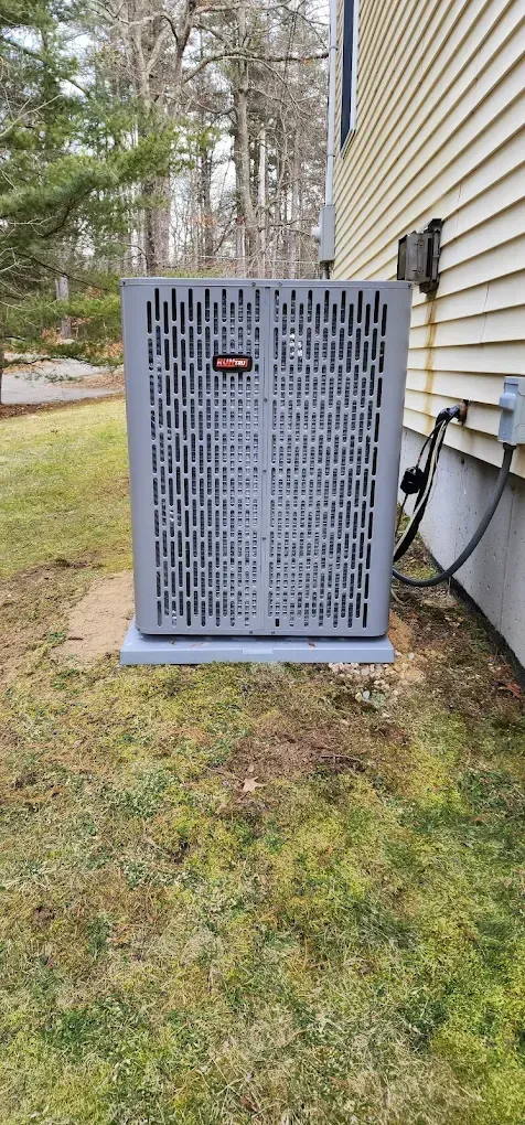 Air conditioning unit next to a house with gray siding, in a yard.