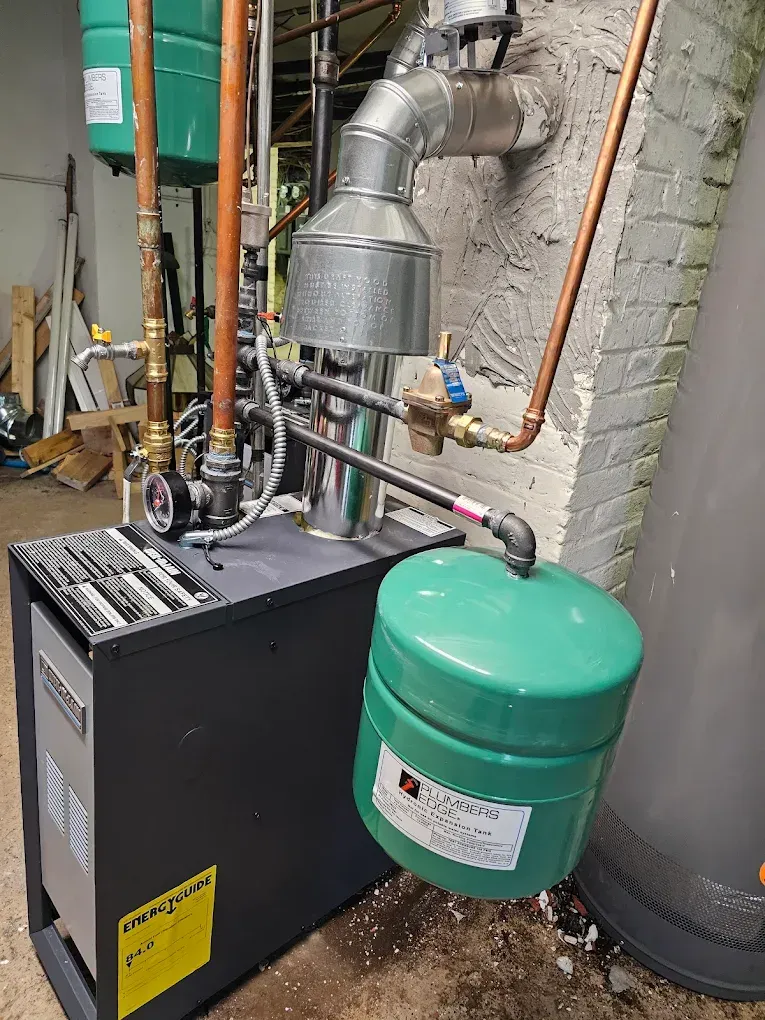 Green and black heating system with copper pipes and a silver exhaust, mounted against a concrete wall.