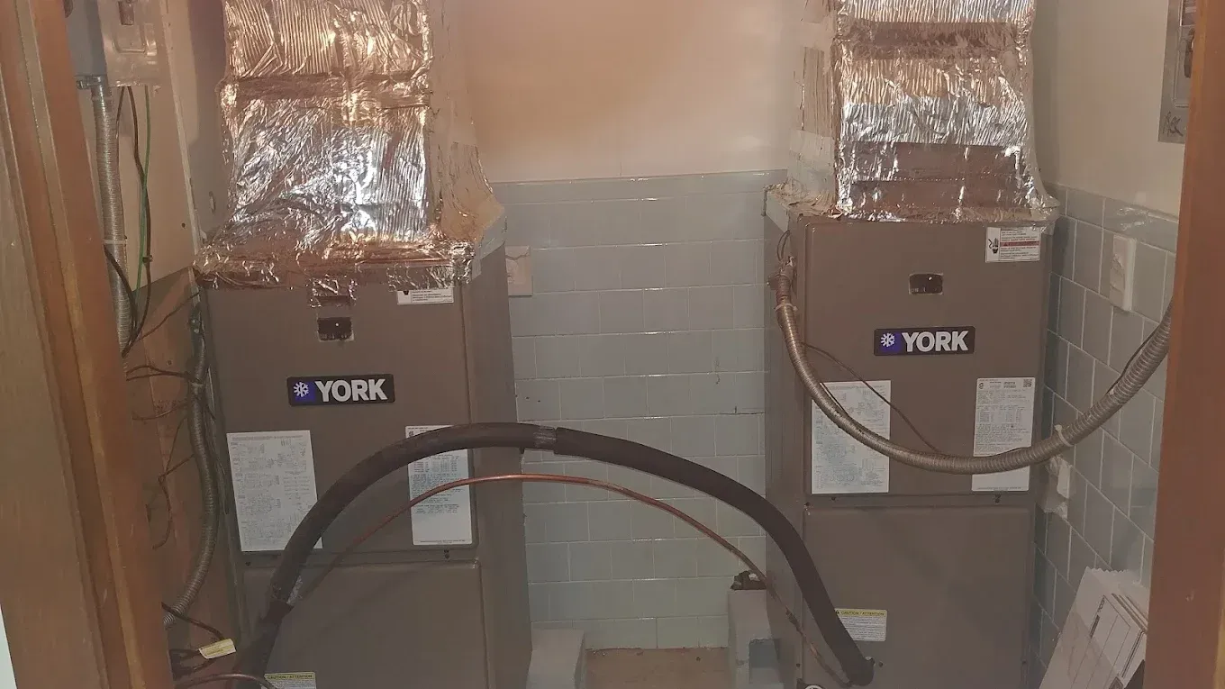 Two York HVAC units side-by-side in a room, ductwork above, copper tubing visible, beige.