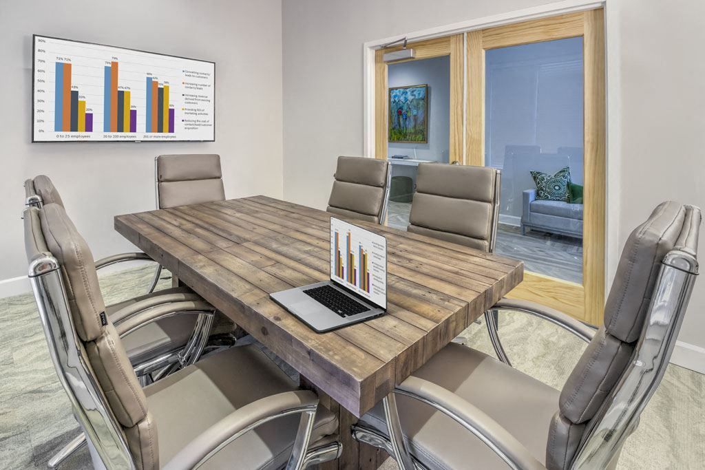 Modern conference room with a wood table, padded chairs, wall chart, and sliding glass doors to a patio