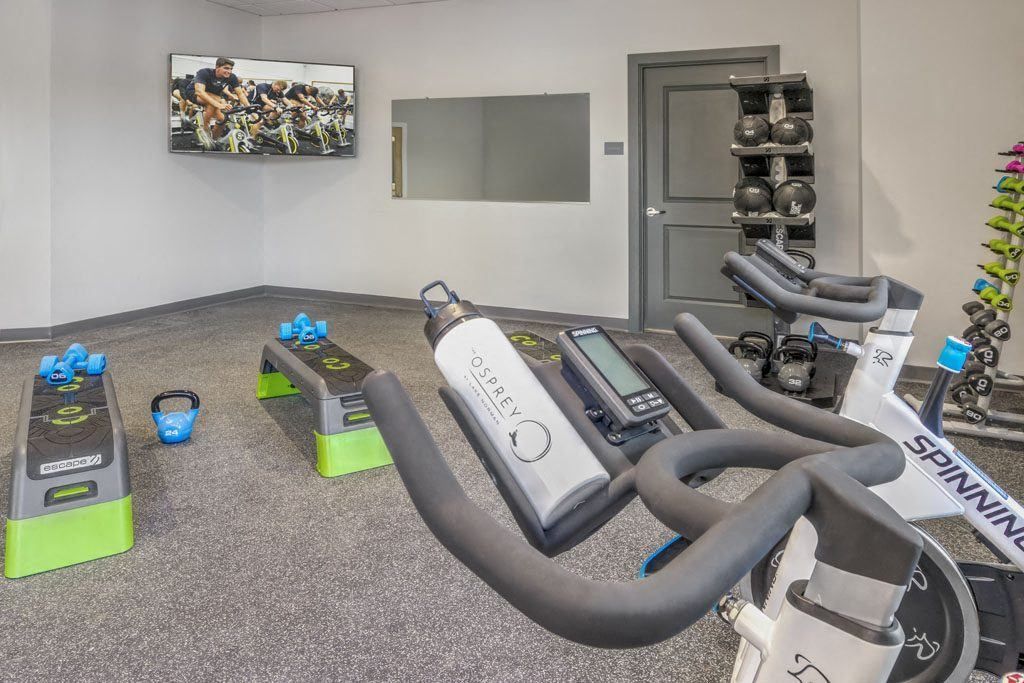 Small indoor fitness studio with exercise bikes, rowing machines, and weight benches on carpeted floor